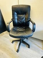 Front view of black leather cushioned office chair showing seat, backrest, armrests and wheeled base
