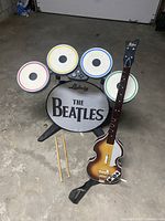 Photo showing full drum controller set with Ludwig branding, four colored drum pads, guitar controller, and two drumsticks on concrete floor.