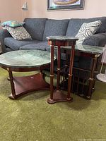 Three vintage marble top end tables displayed in front of a grey couch on green carpet. One is a large round coffee table with dark green marble and wooden base. Another is a rectangular side table with matching marble top and wood base.