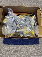 Box of 20 metal vintage oil funnels wrapped individually in plastic, showing yellow and red labels on each funnel.