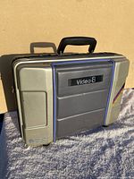 Front and angled view of hard carrying case for Video8 camcorder with handle and 'Video8' label on padded front panel.