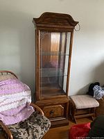 Full view of wood framed glass display cabinet with carved top, glass shelves, and lower wooden storage door.