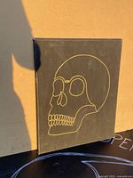 Front view showing black rectangular frame with gold minimal skull outline painting