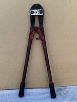 Full view of large bolt cutters showing red handles and black rubber grips on a beige background.