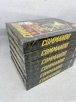 Stack of six sealed Commando Atari 2600 game boxes showing camouflage design and yellow title on spines.