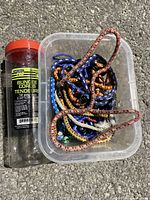 Lot of bungee cords inside a clear plastic container beside an orange-lid storage tube labeled Ouramax Pro.