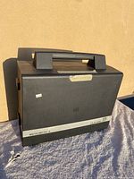 Black carrying case for Micromatic II slide projector with Dukane branding, showing case front and side with handle on top.