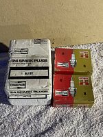 Photo of the three boxes with the folded 24-pack of Champion BL13Y spark plugs and two smaller Champion Autopar boxes, each containing 8 spark plugs.