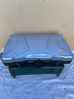 Top view of two stacked Coleman camping stoves, silver stove on top and green stove below.