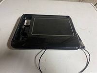 Black uDraw GameTablet with connected cable lying on white surface, including stylus holder on the side.