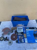 Sanding belts, sanding discs of different kinds, and Norton MetalSand sheets placed around a blue plastic container.