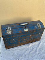 Blue metal toolbox exterior showing rust and paint chipping with carrying handle on top, closed view.