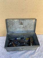 Open metal toolbox showing contents including screwdrivers, clamps, pliers, and other metal hand tools