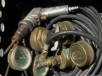 Close-up photo of vintage air zapper handle with multiple pressure gauges and brass fittings connected by black hoses.