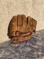 Full view of vintage brown leather baseball glove showing worn condition and button closure.