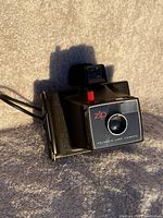 Photo of vintage Polaroid Zip Land Camera showing front and top view including lens, red shutter button, and viewfinder.
