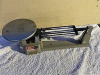 Side angle photo of vintage triple beam balance scale showing metal weighing plate and beam arms