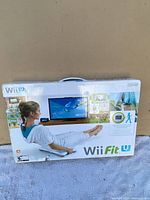 Front of Wii Fit U game box showing a person exercising with the balance board in front of a TV screen.