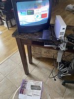 Small CRT TV turned on displaying user interface screen, with Nintendo Wii console and RF modulator on table beside it.