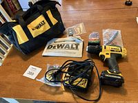 Photo showing the entire set including drill, carrying bag, charger, manual, and accessories laid out on a wooden table.