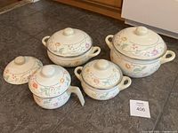 Front view of entire set arranged on floor showing five pots with lids and one extra lid, all featuring floral pattern.