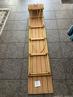 Full length top-down photo of wooden toboggan showing parallel wood slats and yellow rope on tiled floor