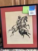 Framed lithograph depicting a matador on horse combating a bull, black and white print with red mat and black frame.