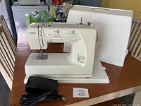 Full view of Kenmore off-white sewing machine model 15512000 with black foot pedal and white hard case behind it on wooden table.
