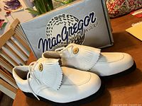 Pair of men's white leather MacGregor golf shoes with decorative fringed kiltie and gold emblem, showing side and top views.