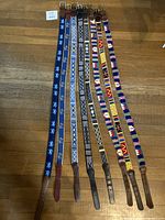 Full view of the eight canvas and leather belts laid out side by side, showing different multicolor patterns and buckle ends.