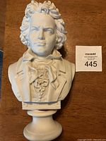Front view of white resin bust of Beethoven, showing detailed curls of hair and facial features on a circular pedestal base with auction lot number beside it.