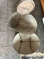 Set of two antique metal hanging scale pans showing full view of pans, chains, and mechanical scale dial attached to one pan with visible rust and wear.