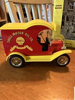 Side view of red and yellow diecast 1912 Ford model car with Shell Motor Oil Co logo and coin bank feature.