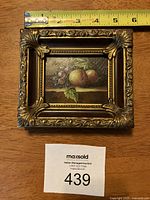 Front view photo of the miniature still life painting in an ornate gilt wood frame with measuring tape showing size approximately 4x3 inches.