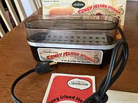 Front view of Sunbeam electric hot dog steamer showing label, power cord, manual and original box behind