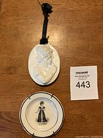 Photo showing both the white plaster miniature wall plaque with black hanging ribbon, and the glazed porcelain decorative plate with image of Miss F. Kemble as Belvidera, placed on wooden surface.