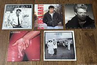 Top-down photo of all 5 vinyl album covers laid out on a wooden surface: Corey Hart's First Offense and Boy In The Box, Bryan Adams Reckless, Loverboy Get Lucky, Honeymoon Suite The Big Prize.