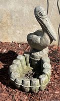 Full view of pelican concrete garden planter showing planter basin and pelican figure with background of mulch and stucco wall