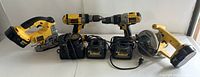 Jigsaw on left, two drills behind, three chargers in front center, circular saw on right
