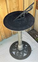 Full view of the plastic sundial mounted on a metal stand with decorative base, showing overall condition and design.