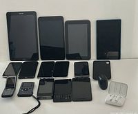Photo of the lot showing all devices front-facing: tablets, smartphones, earbuds, camcorder and phone case.