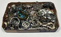 Assorted estate jewelry in a cardboard tray, including bangles, bracelets, necklaces, earrings, and brooches in mixed metal and bead styles.