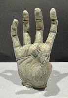 Front view of a greenish textured, jointed hand figurine standing upright with fingers spread.