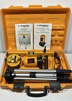 Full kit contents displayed in orange carrying case: laser level, tripod, laser target, safety glasses, spirit level, and manuals.