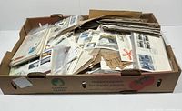 Photo showing a box filled with a large collection of first day covers and covers, some in plastic sleeves and others loose, many with stamps and cancellation marks.