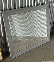 Full view of large rectangular wood framed mirror with beveled glass edges, leaning against a corrugated metal wall, showing minor wear on frame.