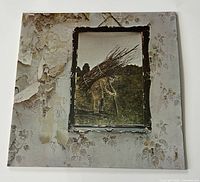Front cover of Led Zeppelin IV LP album featuring damaged peeling wallpaper background with a framed image of a man carrying sticks.