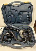 Open carrying case showing black rotary trim-cutter tool with various attachments including cutting guides and metal clamps.