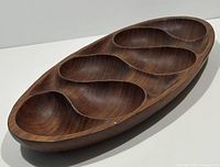 Angled side view showing carved sections and wood grain pattern of oval tray.