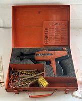 Closed orange metal carrying case with foam interior showing the Ramset D-60 nail tool and fasteners